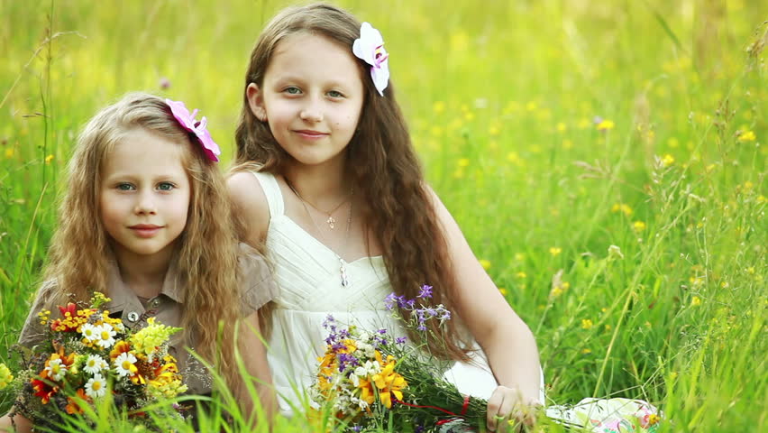 Two sisters sitting on the grass with flowers 