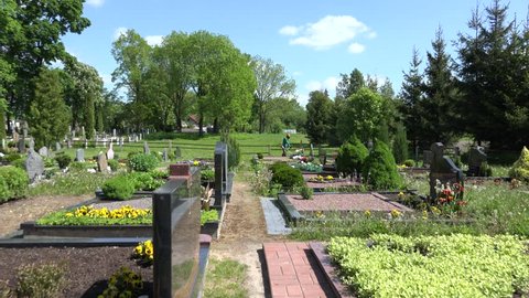 VILNIUS, LITHUANIA - MAY 29, 2015: Cemetery keeper trim grass between graves monuments in spring on May 29, 2015 in Vilnius, Lithuania. Panorama shot. 4K