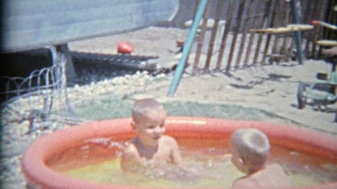 BAKER, CALIFORNIA 1963: Brother intimidating threatening with bucket of water in summer child pool.