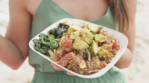 Midsection of woman holding poke salad plate. Closeup of female eating traditional Hawaii dish with raw marinated ahi yellowfin tuna fish at beach. Tourist is representing her healthy lifestyle.
