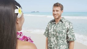 Young woman putting lei garland of pink orchids around man's neck at Hawaiian beach. Handsome male is in Aloha clothing. Happy couple is enjoying their summer vacation.