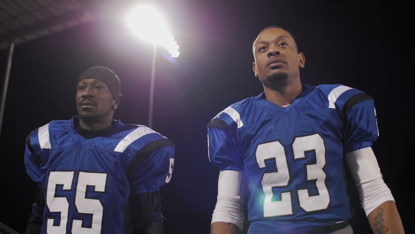 Two football players putting on their helmets and walking onto the field