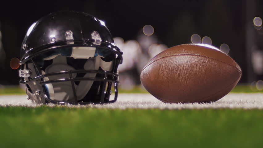 Close up of a football being picked up off the ground with a game going on in the background