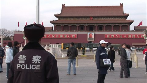 Beijing, China - February 2008: Chinese policeman standing in Tiananmen Square.. Traffic and Mao\x89?s picture at the Tiananmen Gate entrance to the Forbidden City in the background. Beijing, China.