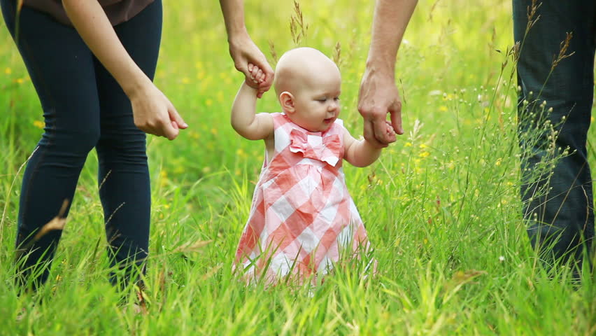 Baby girl learning to walk with parents 
