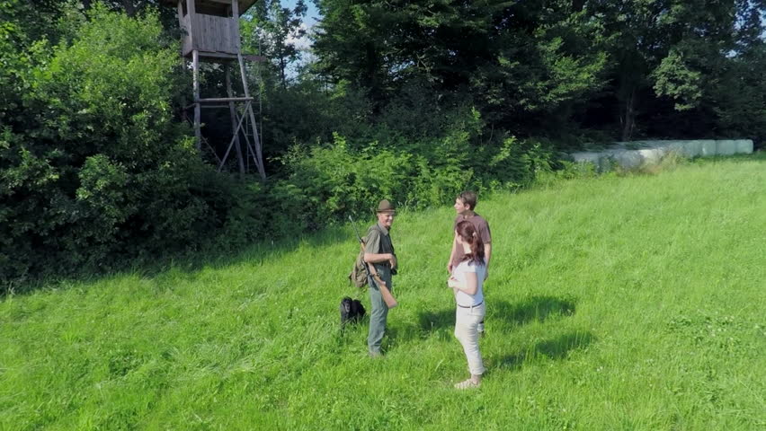 A couple and a hunter goes each own way in a nice green lawn near wood which is pointed on a very natural countryside.