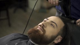 Hairstyling process. Close-up of a barber drying hair of a young bearded man
