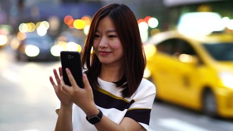 asian woman using app on smartphone smiling and texting on mobile phone. beautiful multicultural young casual female professional on mobile phone. city urban lifestyle background 