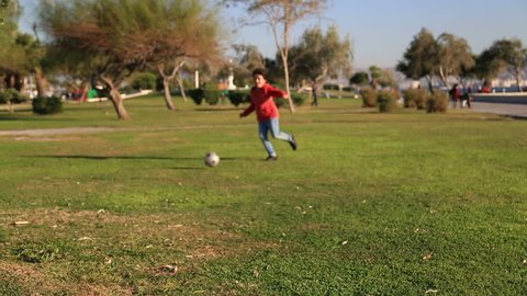 Young boy kicking ball in the grass outdoors