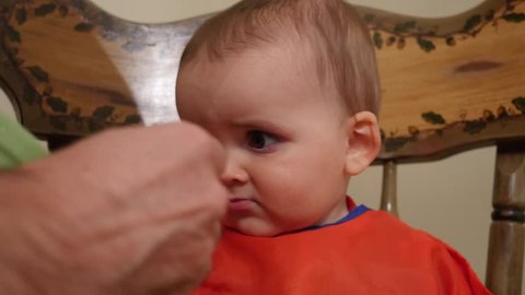 A father attempts to feed his baby boy in the highchair but he wont eat