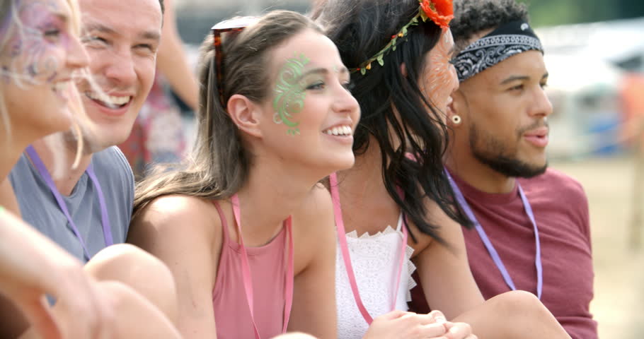 Friends sit on grass talking at a music festival, side view