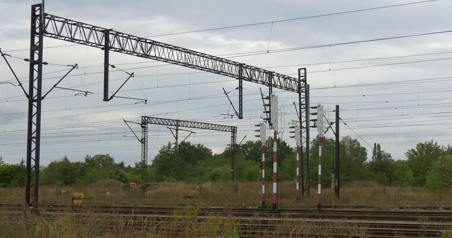 Supports of the railroad contact network, electric wires, lamp posts, input lights. Railroad tracks, rails. Green trees and bushes, dry grass. Grey sky, rain, cloudy autumn day, outdoors. Opole, | Shutterstock HD Video #12603746