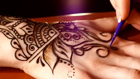 Woman hand being decorated with henna tattoo, mehendi, on black background