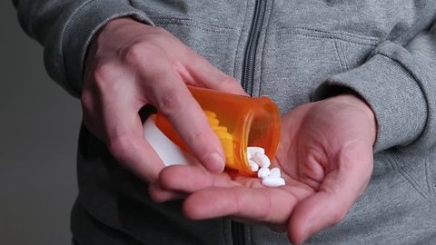 Adult male taking pills. Addiction theme - man pours two pills into the palm of his hand, then decides to take more.