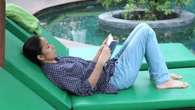 Video Asian woman sits next to the pool and reading book