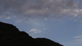 Timelapse clouds moving across evening moon overtop sihouletted mountain