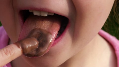 Macro: A little girl is licking chocolate cream from her finger - part 2