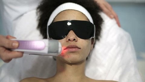 Health and beauty: African american woman have a face whitening procedure. Whitening session with high energy beam of light and chemicals applied to whiten face. Close up