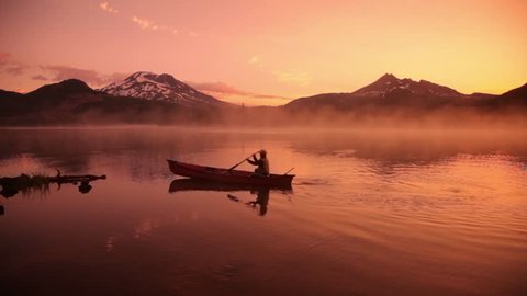 Cinemagraph - Man paddles canoe in lake at sunrise. Motion Photo.