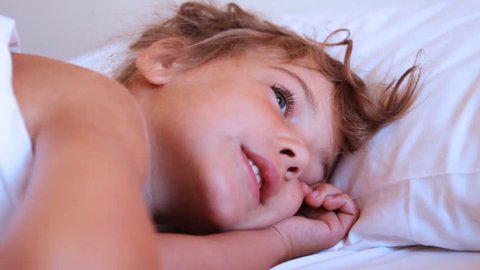 someone trying to wake up cute little smiling girl on pillow