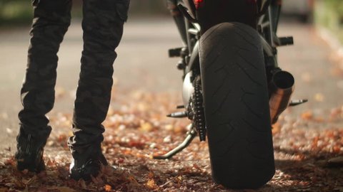 Man Gets on Motorcycle and Rides Away through City Streets with Autumn Leaves.  Male Motorsports Athlete Mounts Black Streetbike and Speeds Off Down Road