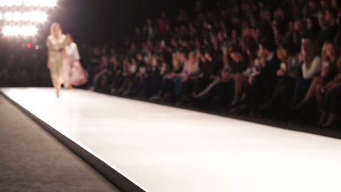 Out of focus background, models walk the runway during fashion show.