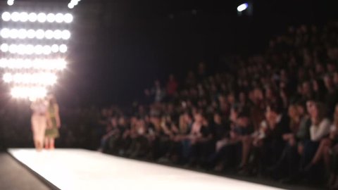 Out of focus background, models walk the runway during fashion show.