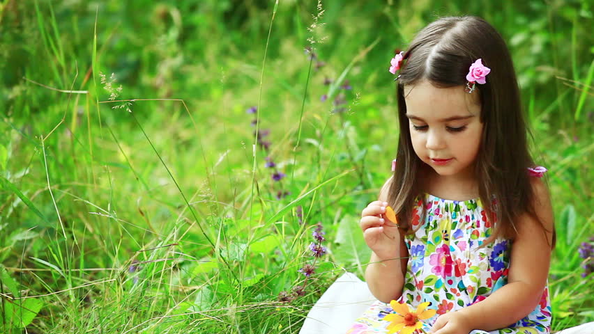 Little girl sitting on the grass she holds a yellow flower 
