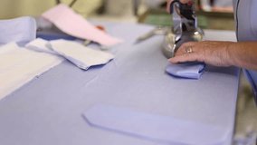 Tailor ironing a blue fabric around a shirt collar band to make a made to measure cotton shirt. 