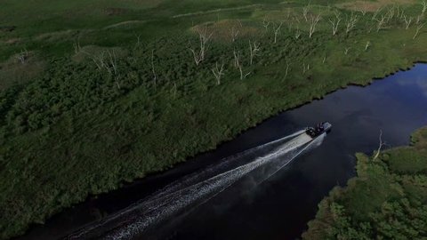 An airboat powers down a waterway just before a southern Louisiana sunset over a bayou and stretch of water dotted with dead trees.
