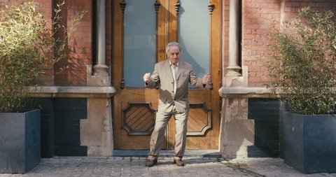 Happy elderly dancer man wearing suit in front of apartment funky street dancing freestyle in the city
