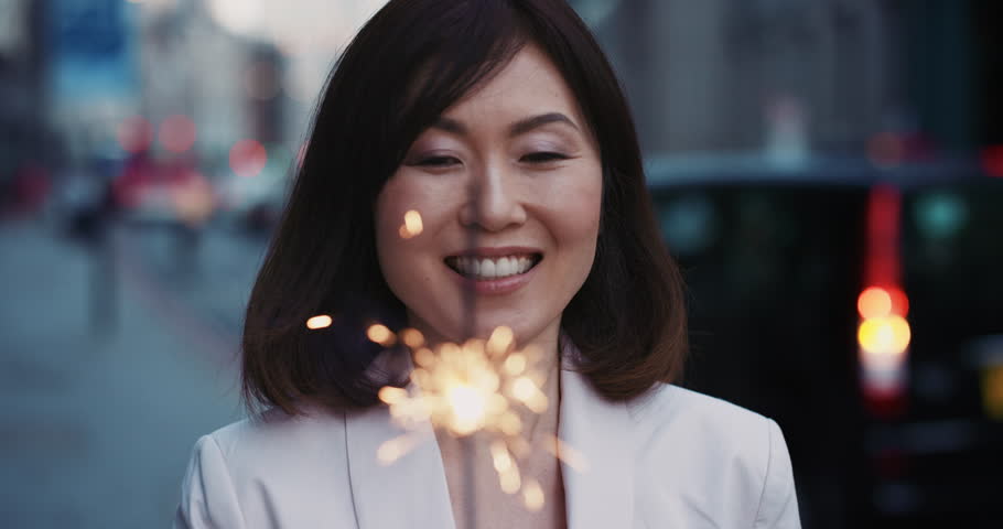 Slow Motion Portrait of beautiful Japanese woman smiling holding sparkler in city celebrating new year success real people series