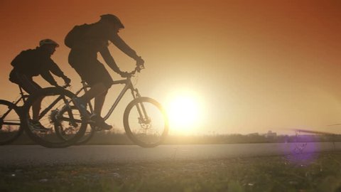 Two people riding bicycles on the background of an orange sunsetting sky