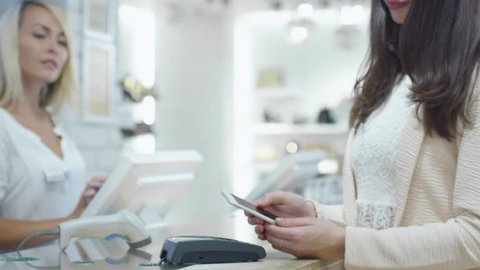 Young woman is paying with her smartphone application at the cash desk in a department store. Shot on RED Cinema Camera in 4K (UHD).