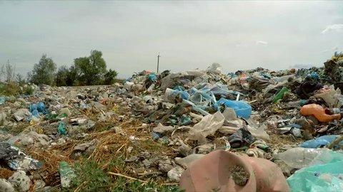 Camera is moving backwards over huge dump of domestic garbage showing closeup of packages swaying on the wind in landfill with cloudy sky on background, environmental problems in Ukraine.
