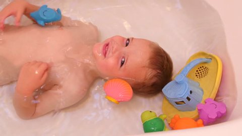 A cute little boy taking a hot bath in a bathtub and playing with his toys