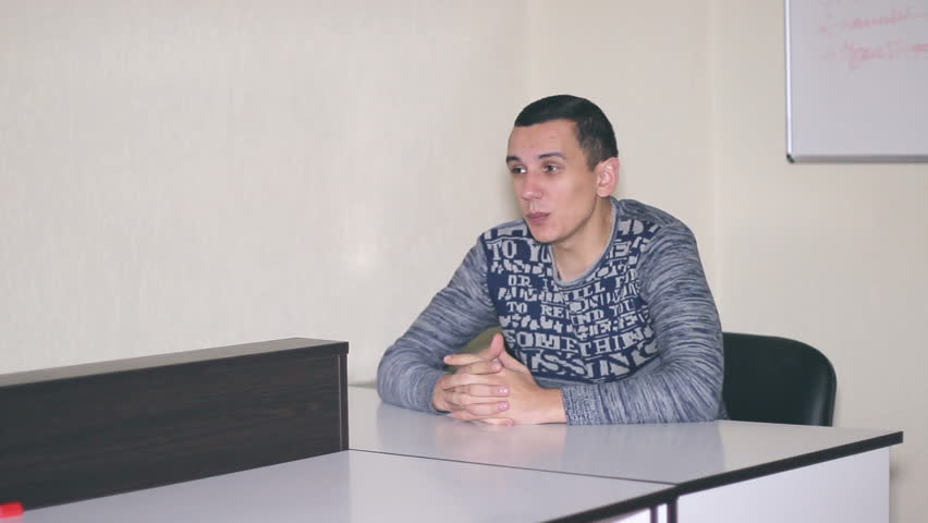 The man sitting in the office at a desk and speech. Man waving his hands showing strength.