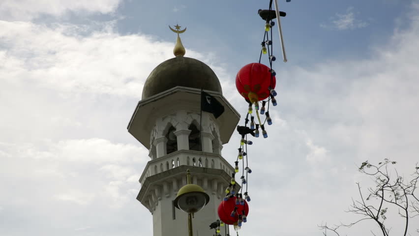 Kapitan Keling Mosque minaret upward view to the top, Chinese lanterns lights with birds above the street, blue sky with clouds, top off tree left bottom corner of frame Penang, Malaysia, day light