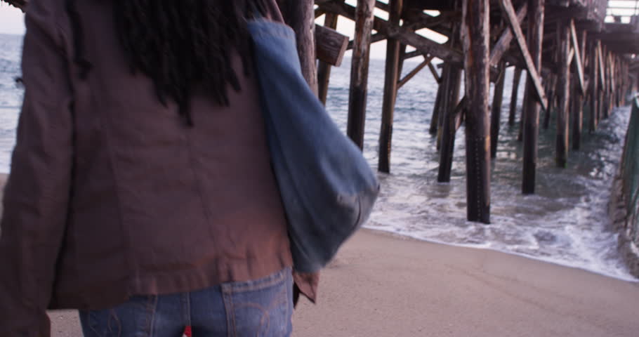 Handheld shot following black women under pier while waves come crashing in