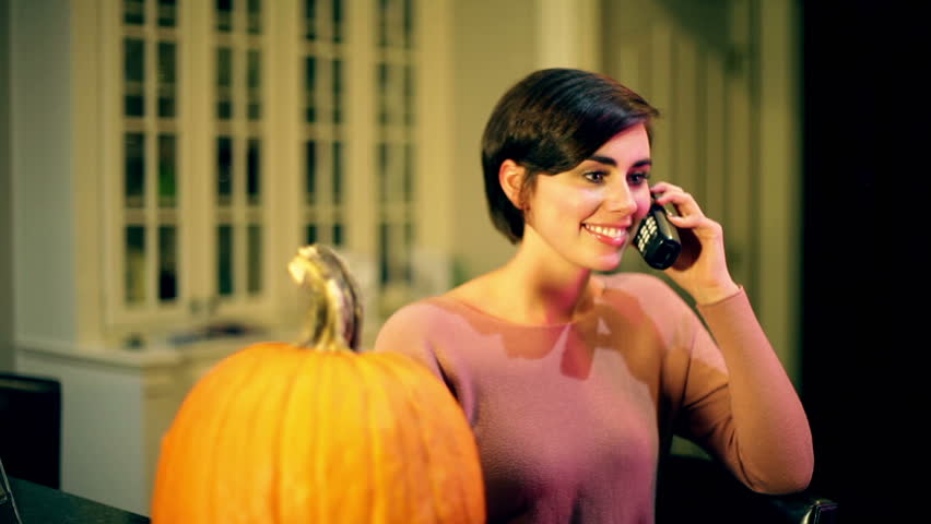 Woman talking on a phone next to a pumpkin