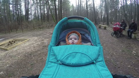 VILNIUS, LITHUANIA - MARCH 11, 2015: Curious newborn baby in stroller on March 11, 2015 in Vilnius, Lithuania. People spent time in park playground with kids in spring. Wide angle POV shot. 4K UHD. Redaktionell stockvideo