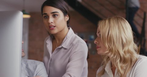 Woman team leader meeting with diverse group of startup business people pointing at computer screen in trendy modern office with red brick walls slow motion