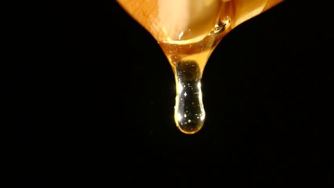Thick honey dripping from the honey spoon, one drop, on black background, close up
