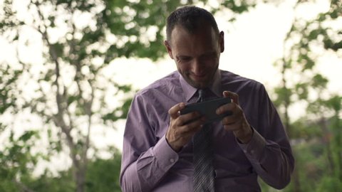 Young businessman playing game on smartphone in park, slow motion 240fps
