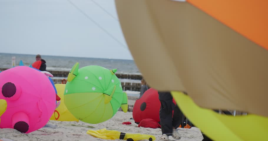 LEBA/POLAND - AUG 28 2015: Air swimmers shaped like animals are connected with a string and bouncind in the sand. People are preparing to fly their kites in the air or already flying them in the sand | Shutterstock HD Video #12729461