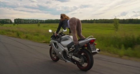 Sexy woman biker shaking her hips and riding motorcycle at the same time