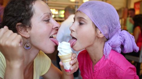 Happy mother and daughter lick sweet ice cream in cafe