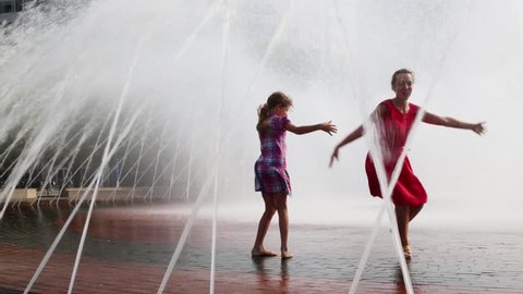 Happy mother and daughter dance in fountain on street