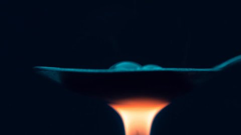 The spoon boiling drug heroin is heated by the flame of a lighter on black background. Closeup. Shallow depth of field