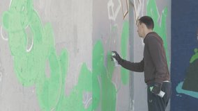 Guy with spray draws graffiti on wall. Performance,raw video,no grading. Talented graffiti artist painting. Young man spraying graffiti on wall with spray bottle. Male painter performing street art.